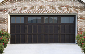 Black paneled garage door with small windows in the top, on a light tan brick home.