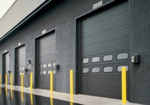 Row of commercial garage doors in the side of a black warehouse building.