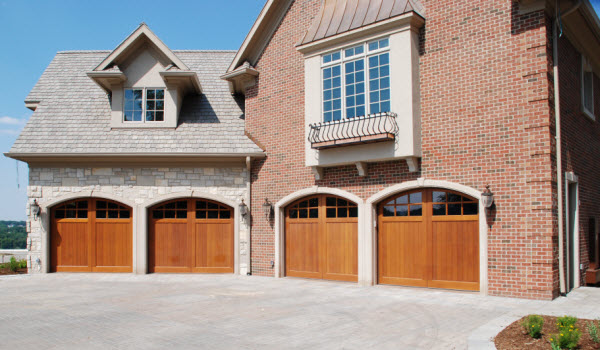 Four carriage style wooden garage doors from Signature in a large brick home.