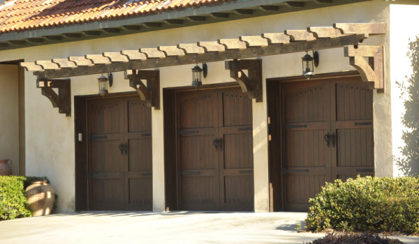 Carriage style wooden garage doors from Signature, on a white stucco home.